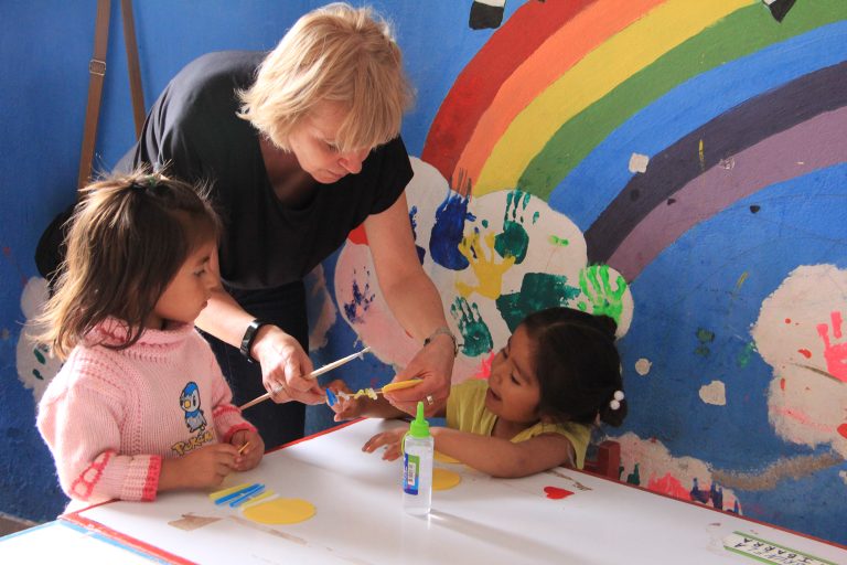 Volunteer painting with children in front of a rainbow mural