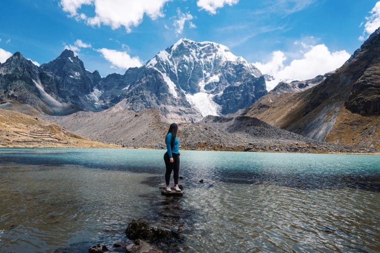 Volunteer standing by a glacial lake beneath snow-capped Andes peaks near Cusco