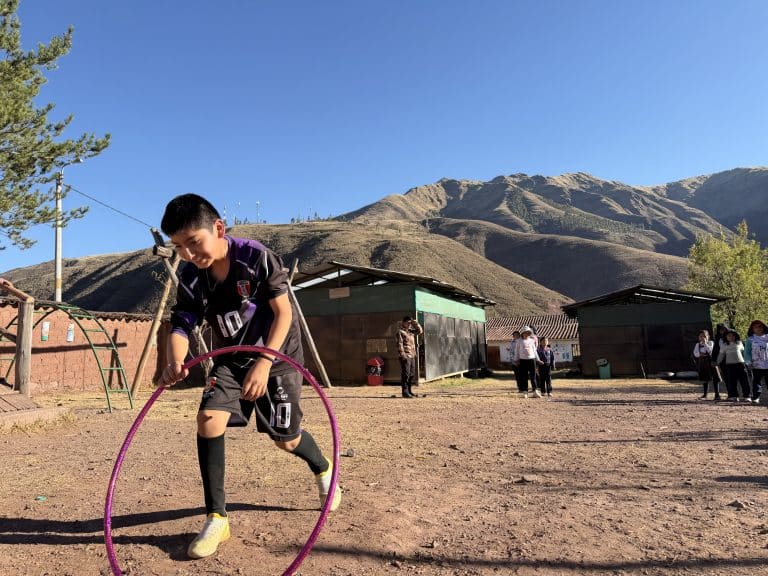 A boy stepping through a hula hoop in the schoolyard near Cusco