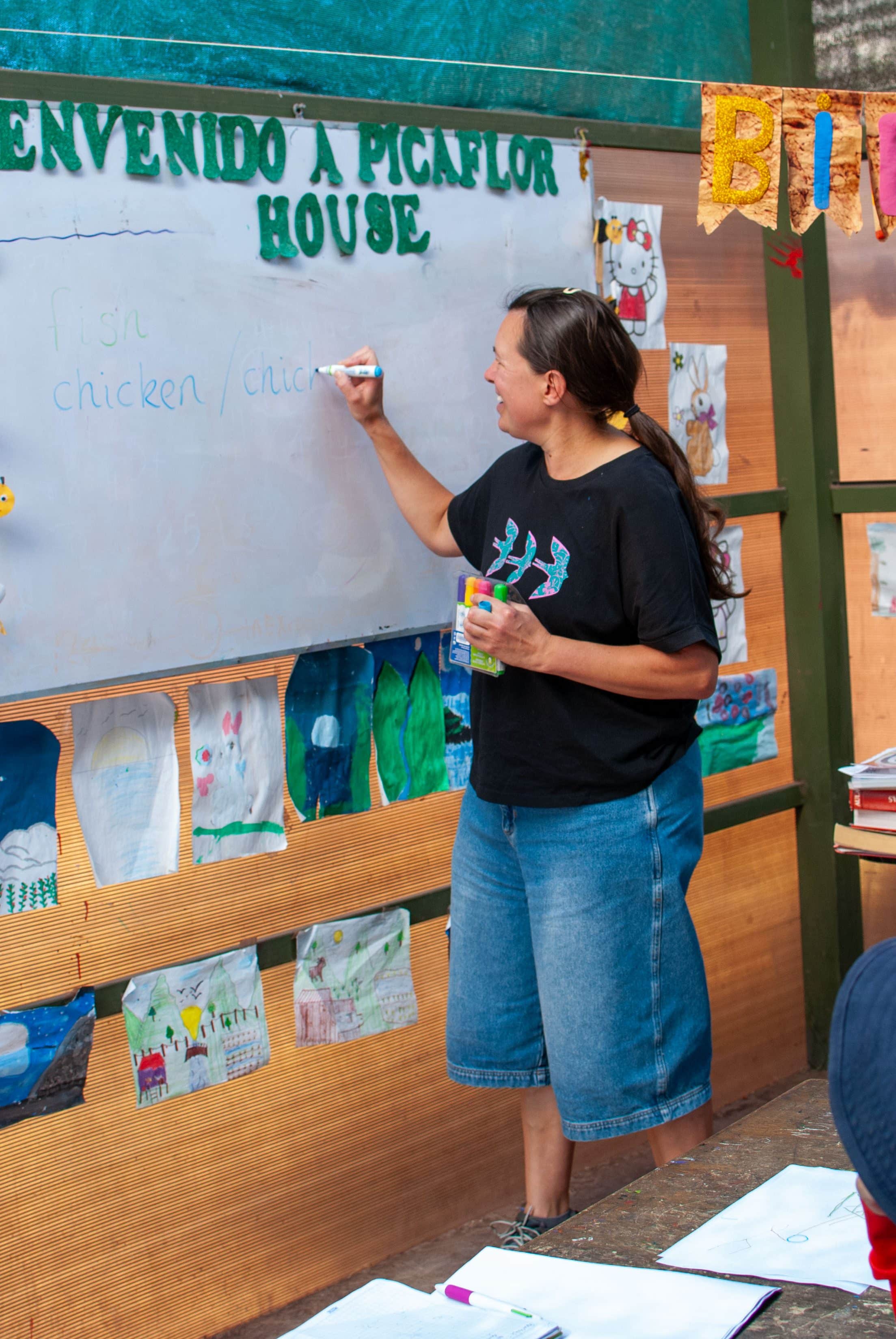 Volunteer in a black T-shirt writing on a whiteboard under a sign reading Bienvenido a Picaflor House