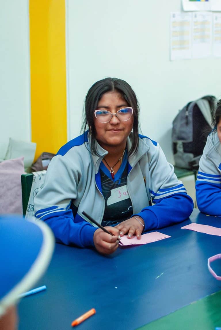Girl in glasses writing during a classroom activity in Cusco