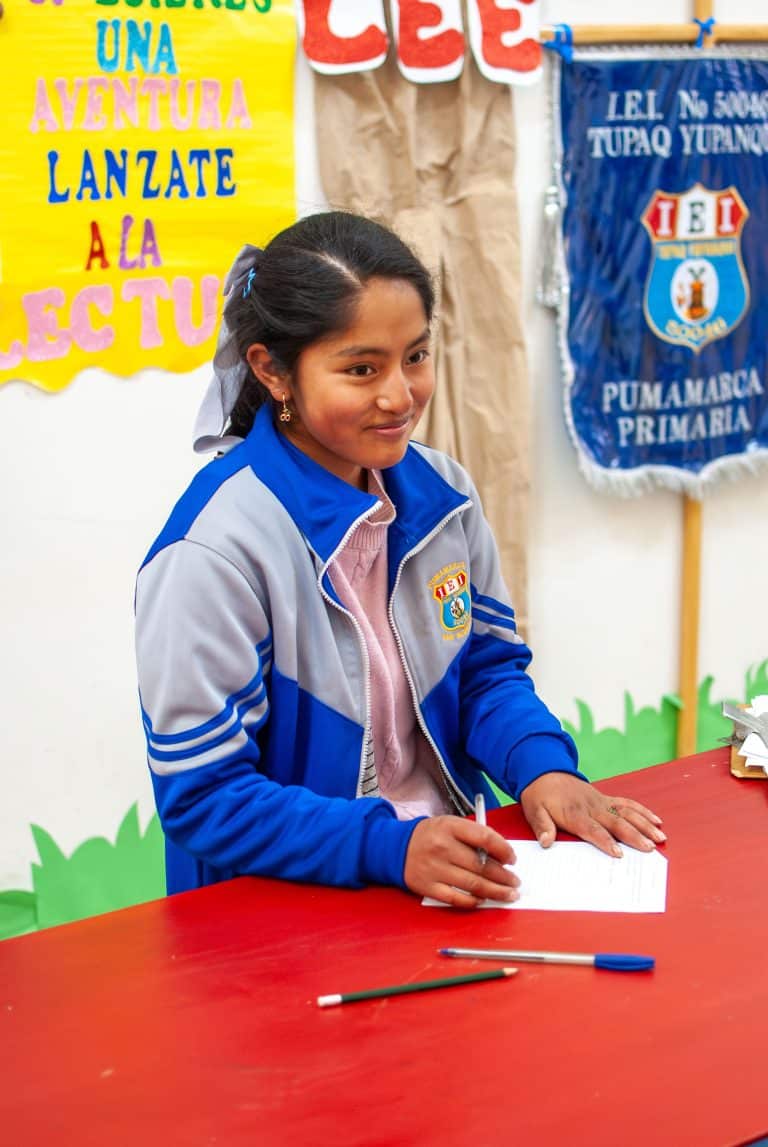 Smiling schoolgirl writing at a red table in Cusco