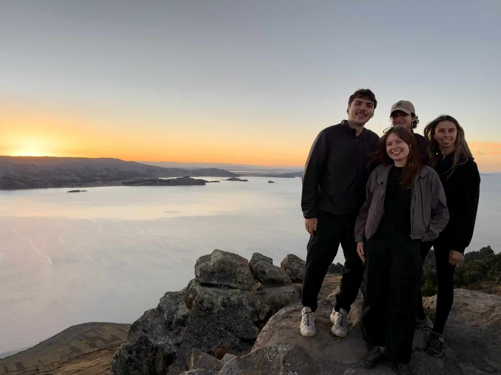Four Globalteer volunteers smiling on a rocky viewpoint above Lake Titicaca at sunset