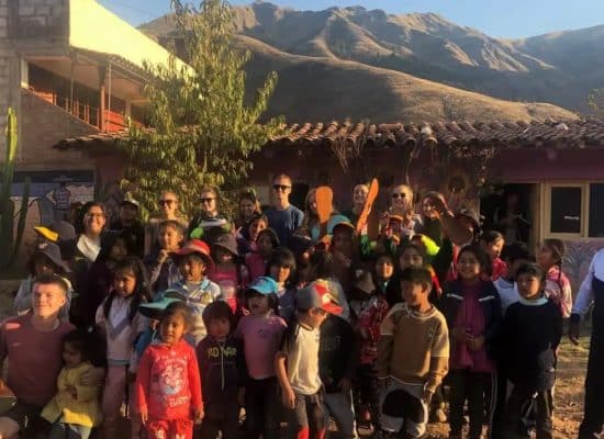 Volunteers and children together outside Picaflor House, with the mountains near Cusco behind"