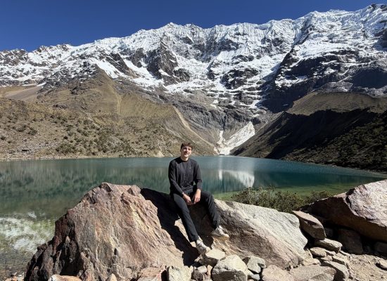 Volunteer sitting on a rock at Humantay Lake below a snow-covered mountain near Cusco"