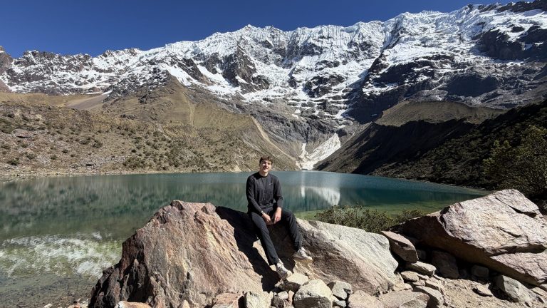 Volunteer sitting on a rock at Humantay Lake below a snow-covered mountain near Cusco