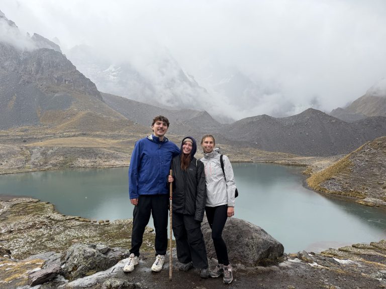 Three volunteers in front of a turquoise mountain lake in the Ausangate area, Peru