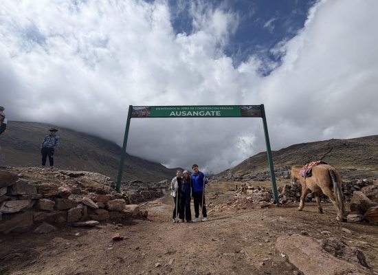 Three volunteers under the Ausangate conservation area sign near Cusco"