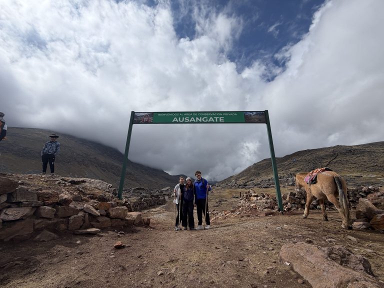 Three volunteers under the Ausangate conservation area sign near Cusco